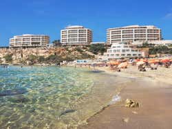 A sandy beach under a blue sky with buildings along the coast